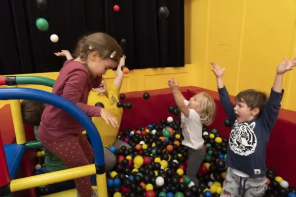 Vier kleine Kinder spielen und werfen Bälle in einer Ballgrube mit gelben und roten Wänden.