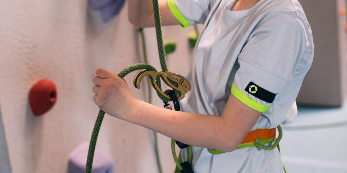 Ein junges Mädchen, das einen Klettergurt trägt, bereitet ein Kletterseil mit einem Sicherungsgerät in einer Kletterhalle vor.