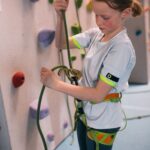 Ein junges Mädchen, das einen Klettergurt trägt, bereitet ein Kletterseil mit einem Sicherungsgerät in einer Kletterhalle vor.