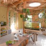 Ein sonnendurchfluteter Raum mit Holzbalken, einem Fischbecken, Mikroskopen auf einem Tisch, verschiedenen Pflanzen, Regalen mit Büchern und runden Fenstern in den Wänden.