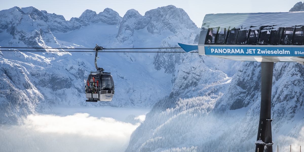 Eine Gondelbahn mit der Aufschrift "Panorama Jet Zwieselalm" befördert die Fahrgäste über eine verschneite Berglandschaft mit schroffen Gipfeln im Hintergrund.
