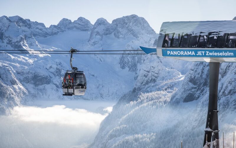 Eine Gondelbahn mit der Aufschrift "Panorama Jet Zwieselalm" befördert die Fahrgäste über eine verschneite Berglandschaft mit schroffen Gipfeln im Hintergrund.
