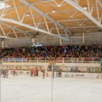 Ein Eishockeyspiel in einer Halle mit Spielern auf der Eisfläche und einer großen Zuschauermenge auf der Tribüne.