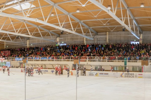 Ein Eishockeyspiel in einer Halle mit Spielern auf der Eisfläche und einer großen Zuschauermenge auf der Tribüne.