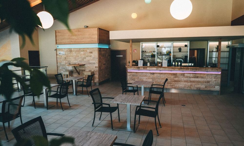 Modernes Café-Interieur mit leeren schwarzen Stühlen und quadratischen Tischen, gefliestem Boden, minimalistischem Dekor und sanfter Deckenbeleuchtung. Der Thekenbereich ist im Hintergrund zu sehen.
