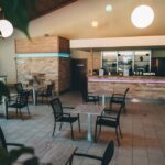 Modernes Café-Interieur mit leeren schwarzen Stühlen und quadratischen Tischen, gefliestem Boden, minimalistischem Dekor und sanfter Deckenbeleuchtung. Der Thekenbereich ist im Hintergrund zu sehen.