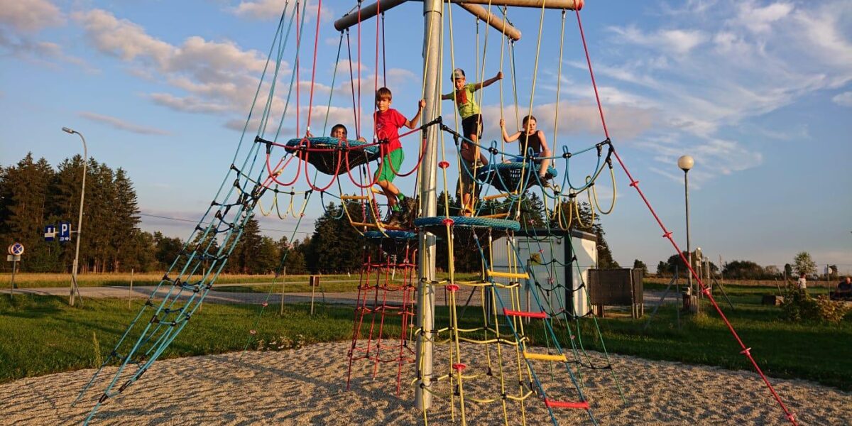 Vier Kinder klettern und spielen an einem sonnigen Tag auf einem Seilklettergerüst auf einem Spielplatz im Freien.