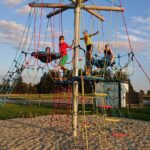Vier Kinder klettern und spielen an einem sonnigen Tag auf einem Seilklettergerüst auf einem Spielplatz im Freien.