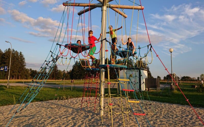 Vier Kinder klettern und spielen an einem sonnigen Tag auf einem Seilklettergerüst auf einem Spielplatz im Freien.
