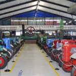 In einer großen Ausstellungshalle mit deutschen Schildern über den Exponaten sind reihenweise alte Traktoren und Maschinen ausgestellt.