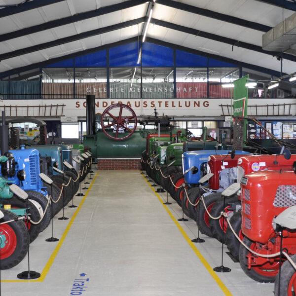 In einer großen Ausstellungshalle mit deutschen Schildern über den Exponaten sind reihenweise alte Traktoren und Maschinen ausgestellt.