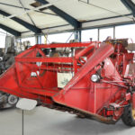Ein alter roter Mähdrescher ist in einem Museum ausgestellt, umgeben von anderen antiken Landmaschinen.