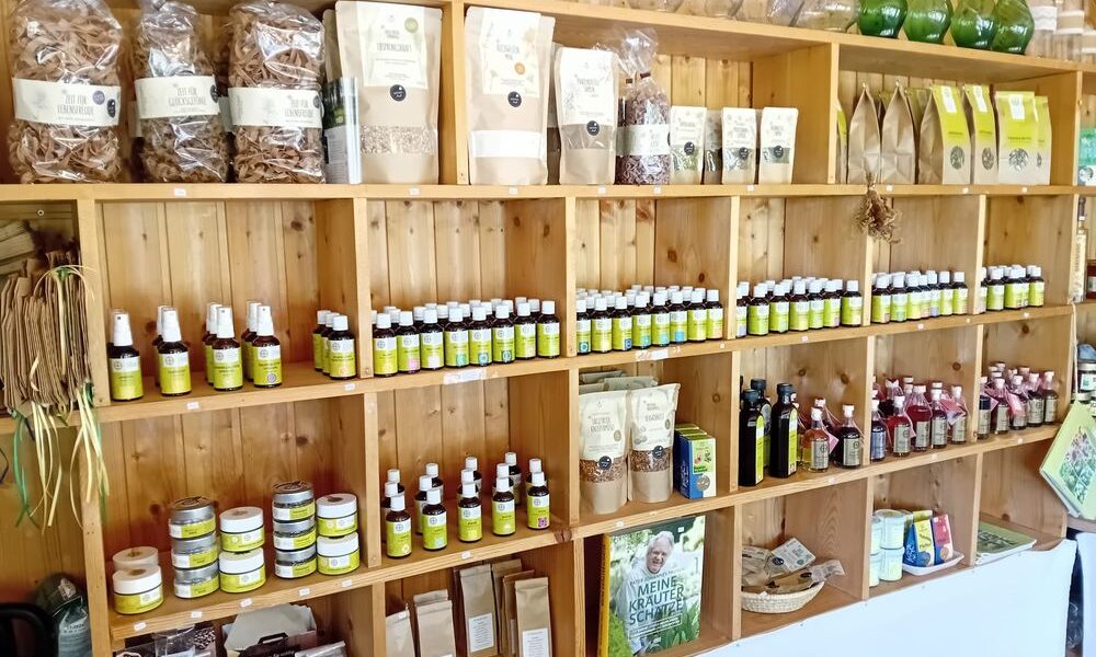 In Holzregalen werden verschiedene Naturprodukte wie Gläser, Flaschen, Päckchen und getrocknete Kräuter in einem Laden ausgestellt.
