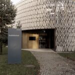 Ein modernes rundes Gebäude mit einer gemusterten Fassade mit der Aufschrift "Stadtbibliothek"; ein Schild und ein Kopfsteinpflasterweg führen zum Eingang.