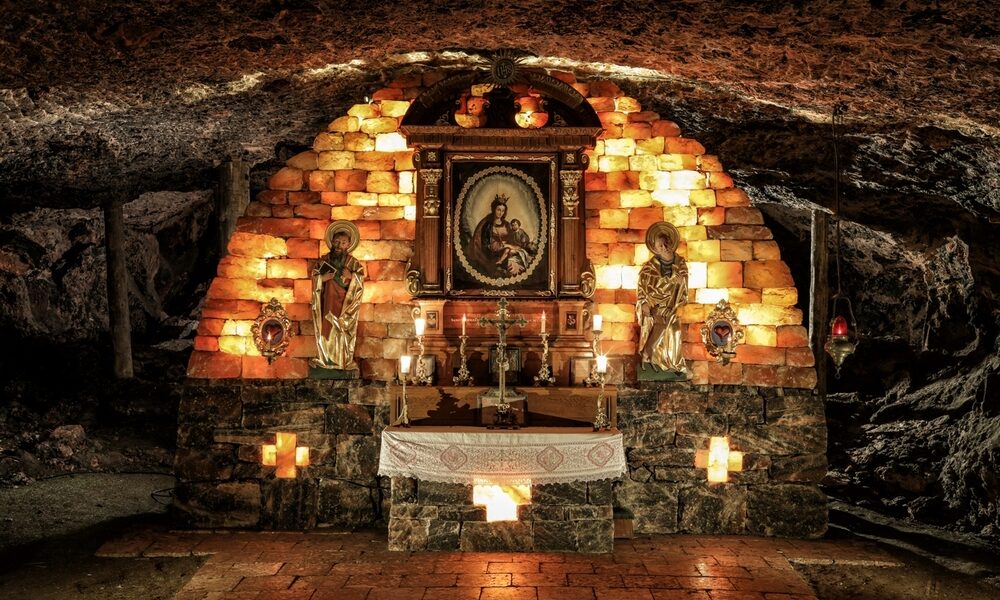 Eine unterirdische Kapelle mit einem Steinaltar, religiösen Statuen, brennenden Kerzen und einem gerahmten Gemälde in der Mitte, das an einer gewölbten Ziegelwand hängt.