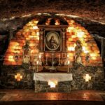 Eine unterirdische Kapelle mit einem Steinaltar, religiösen Statuen, brennenden Kerzen und einem gerahmten Gemälde in der Mitte, das an einer gewölbten Ziegelwand hängt.
