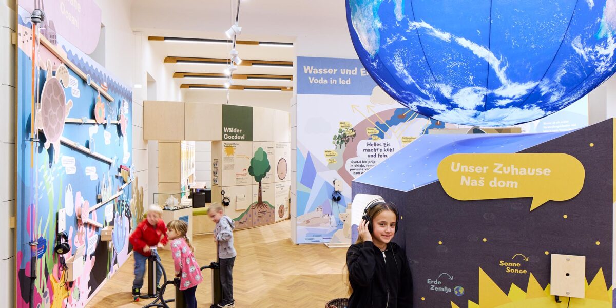 In einem hell beleuchteten Raum, in dem ein Globus an der Decke hängt und informative Schilder über die Erde und das Wasser zu sehen sind, können Kinder interaktive naturwissenschaftliche Exponate erkunden.