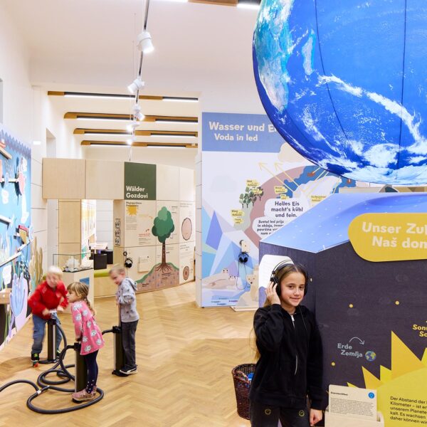 In einem hell beleuchteten Raum, in dem ein Globus an der Decke hängt und informative Schilder über die Erde und das Wasser zu sehen sind, können Kinder interaktive naturwissenschaftliche Exponate erkunden.