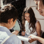 Eine Gruppe junger Menschen versammelt sich im Freien und schaut sich gemeinsam ein Klemmbrett oder ein Stück Papier an und schreibt darauf.