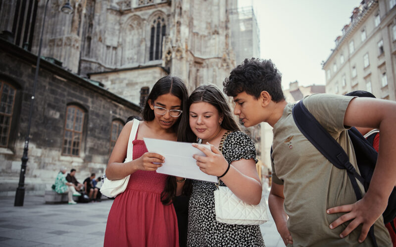 Drei Teenager stehen gemeinsam vor einem historischen Gebäude und schauen auf einen Tablet-Bildschirm.