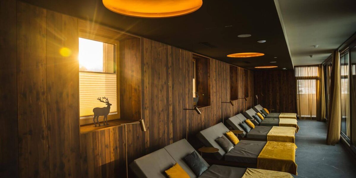 Ein Lounge-Bereich mit Holzwänden, mehreren gepolsterten Sesseln mit gelben Decken und Sonnenlicht, das durch ein Fenster fällt.