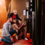 Vier Personen unterschiedlichen Alters interagieren mit einem Touchscreen und Kopfhörern in einer schwach beleuchteten Ausstellung oder einem Museum.