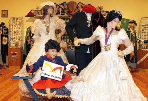 Eine Ausstellung von Schaufensterpuppen in aufwändigen Kostümen, darunter Hochzeitskleider und ein Kinderkostüm, in einem dekorierten Innenraum des Museums.