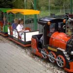 Ein kleiner Vergnügungspark mit mehreren Kindern, die in den bunten Waggons sitzen und bereit sind, über einen gepflasterten Weg abzufahren.