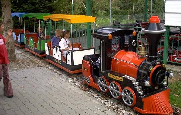 Ein kleiner Vergnügungspark mit mehreren Kindern, die in den bunten Waggons sitzen und bereit sind, über einen gepflasterten Weg abzufahren.