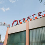 Gebäude des Pratermuseums mit Teilansicht des Wiener Riesenrads im Hintergrund, bei klarem Himmel und umgeben von Bäumen.