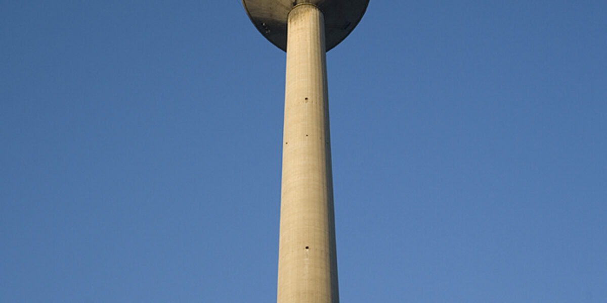 Ein hoher Fernmeldeturm aus Beton mit einer Aussichtsplattform erhebt sich in den klaren blauen Himmel.