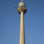 Ein hoher Fernmeldeturm aus Beton mit einer Aussichtsplattform erhebt sich in den klaren blauen Himmel.