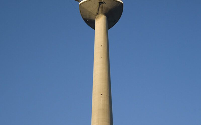 Ein hoher Fernmeldeturm aus Beton mit einer Aussichtsplattform erhebt sich in den klaren blauen Himmel.