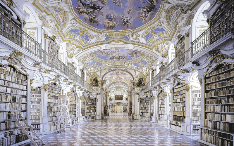 Prunkvolle Bibliothek mit hohen Gewölbedecken, kunstvollen Fresken, hohen, mit Büchern gefüllten Regalen und schachbrettartigen Marmorböden. Entlang der Regale sind Leitern angebracht, die den Zugang erleichtern.