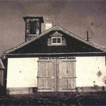 Ein Schwarz-Weiß-Foto eines kleinen, alten Feuerwehrgebäudes mit doppelten Holztüren und einem Glockenturm über dem Eingang.