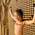 Zwei junge Mädchen spielen mit einer großen interaktiven Wand aus Holzpflöcken und drücken ihre Körper in die Pflöcke, um Abdrücke ihrer Umrisse zu erzeugen.