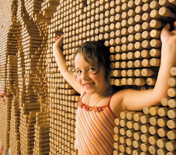 Zwei junge Mädchen spielen mit einer großen interaktiven Wand aus Holzpflöcken und drücken ihre Körper in die Pflöcke, um Abdrücke ihrer Umrisse zu erzeugen.