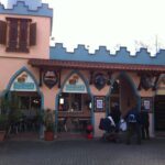 Ein Restaurant mit einer schlossähnlichen Fassade, gewölbten Eingängen und Schildern mit der Aufschrift "Sindbad's Burger Restaurant". In der Nähe des Eingangs stehen Menschen mit einem Kinderwagen.