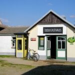 Kleines ländliches Gebäude mit einem „Gasthaus“-Schild, einer gelben Telefonzelle, einem davor geparkten Fahrrad und einem Bitburger-Bier-Schild an der Wand.
