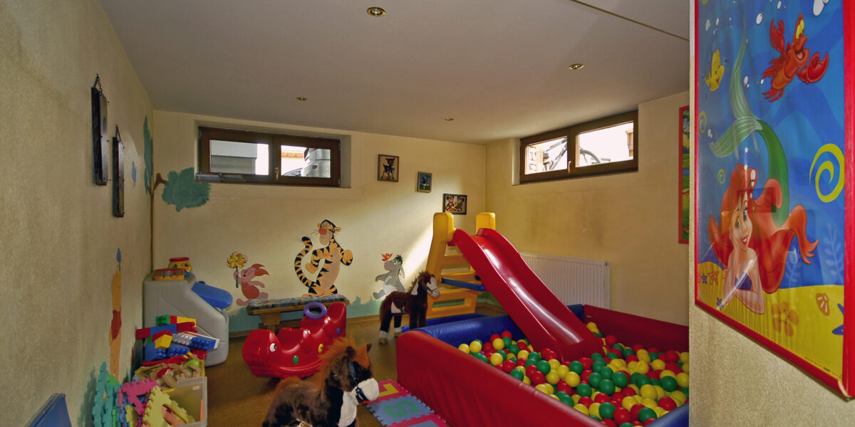 Ein Kinderspielzimmer mit einer Ballgrube, einer Rutsche, einem Schaukelpferd, Spielzeug, einer Buchstabenmatte aus Schaumstoff und bunten Wanddekorationen.