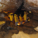 Mehrere Personen mit gelben Regenmänteln und Helmen stehen in einer Felshöhle, die von künstlichen Lichtern beleuchtet wird.