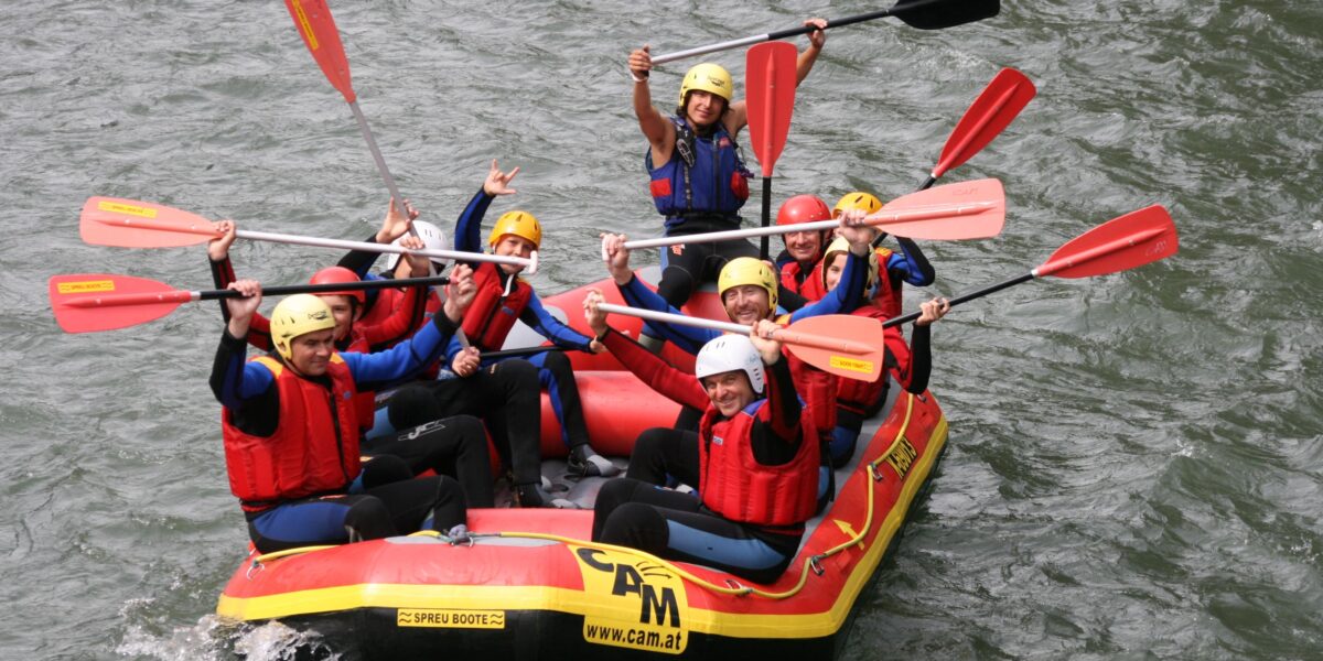 Eine Gruppe von Personen mit Helmen und Schwimmwesten paddelt auf einem aufblasbaren Floß in einem Fluss und posiert für die Kamera.
