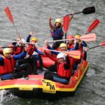 Eine Gruppe von Personen mit Helmen und Schwimmwesten paddelt auf einem aufblasbaren Floß in einem Fluss und posiert für die Kamera.