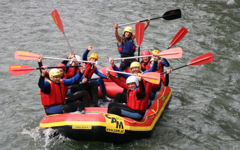 Eine Gruppe von Personen mit Helmen und Schwimmwesten paddelt auf einem aufblasbaren Floß in einem Fluss und posiert für die Kamera.