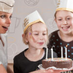Vier Kinder und ein Erwachsener mit Papierhüten haben sich um einen kleinen Schokoladenkuchen mit brennenden Kerzen versammelt und bereiten sich darauf vor, diese gemeinsam auszublasen.