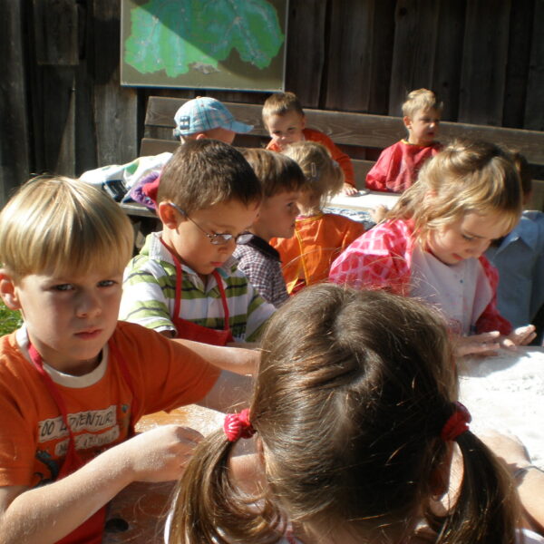 Eine Gruppe kleiner Kinder sitzt im Freien an einem Tisch und beschäftigt sich mit weißem, pulverförmigem Material.