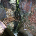Holzstege führen durch eine enge, felsige Schlucht mit steilen Steinwänden und spärlichem Grün darüber.