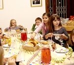 Eine Gruppe Kinder sitzt mit Essen und Getränken um einen dekorierten Tisch herum und scheint eine Party im Haus zu feiern.
