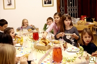Eine Gruppe Kinder sitzt mit Essen und Getränken um einen dekorierten Tisch herum und scheint eine Party im Haus zu feiern.
