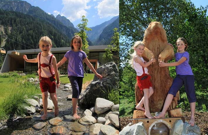 Zwei Mädchen posieren im Freien; auf dem ersten Foto stehen sie auf Felsen neben einem modernen Gebäude und Bergen, und auf dem zweiten halten sie sich an einer großen geschnitzten Tierstatue fest.